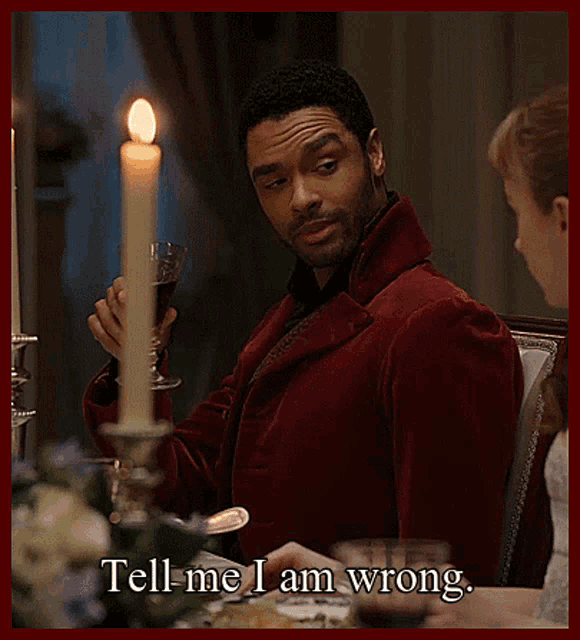 a man in a red jacket is holding a glass of wine and says tell me i am wrong .