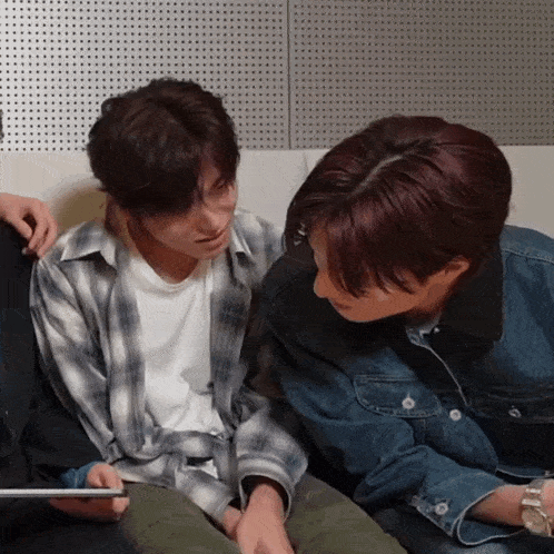 two young men are sitting on a couch looking at something