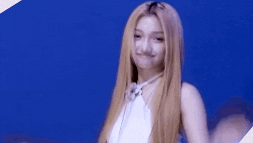 a woman with long blonde hair is wearing a white top and making a funny face .