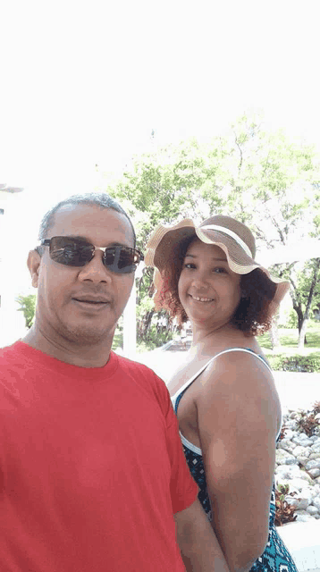 a man in a red shirt and a woman in a straw hat are posing for a picture