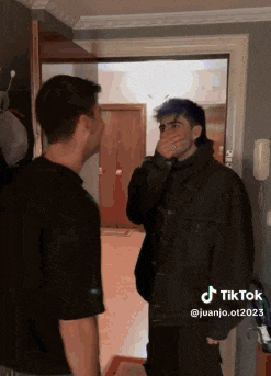 a man with blue hair is covering his mouth while standing next to another man in a black jacket .