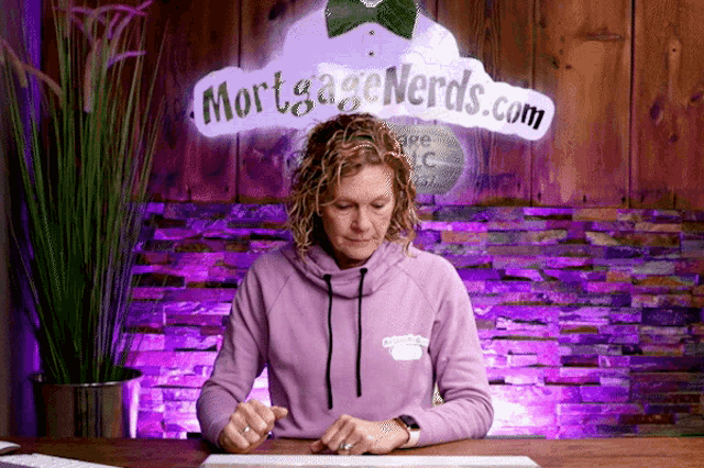 a woman is sitting at a desk in front of a sign that says " mortgage nerds.com "