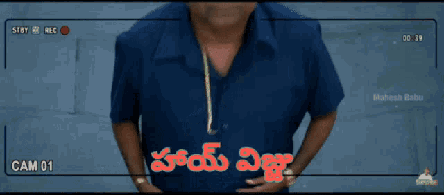 a man in a blue shirt stands in front of a camera that says cam 01 on it