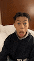 a young boy is sitting on a bed with his mouth open and making a funny face .