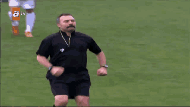 a man with a mustache is running on a field with a tv logo behind him
