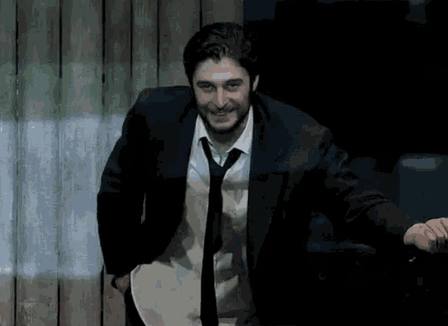 a man in a suit and tie is smiling while standing in a dark room .