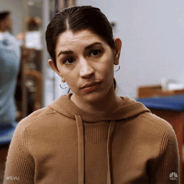 a woman wearing a brown sweater and hoop earrings is looking at the camera ..