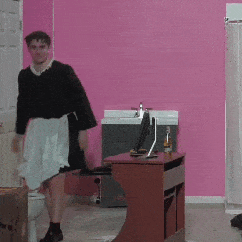 a man is standing in front of a desk with a computer and a bottle of corona on it