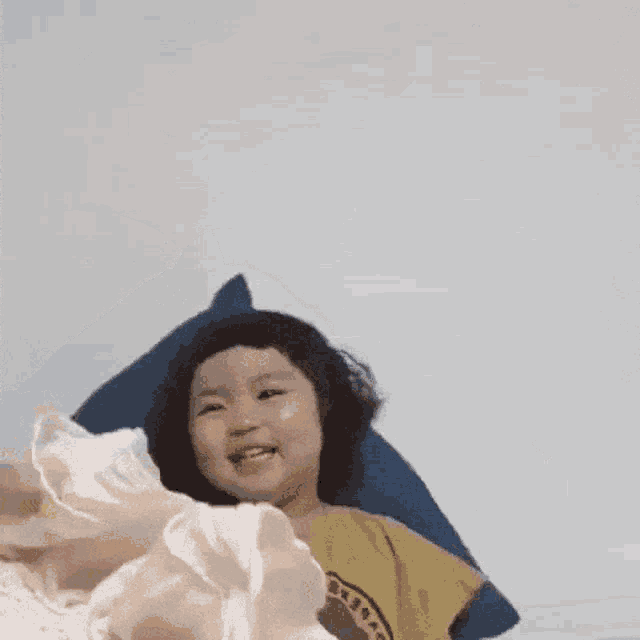 a little girl is laying on a bed with a pillow and a blanket .