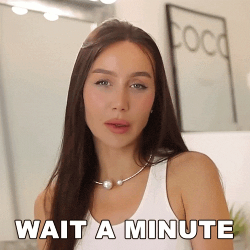 a woman is wearing a white tank top and a pearl necklace and says wait a minute