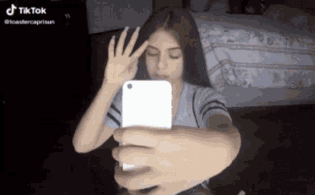 a girl is taking a selfie with her phone and making a hand gesture .