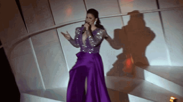 a woman in a long purple dress sings into a microphone