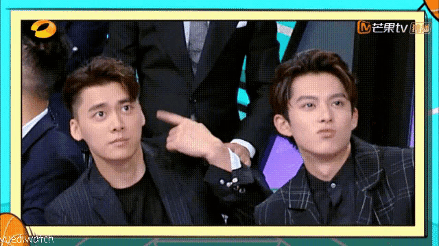 two men in suits are sitting next to each other and one of them is pointing at the other .