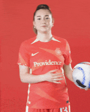 a woman wearing a red providence jersey holds a soccer ball