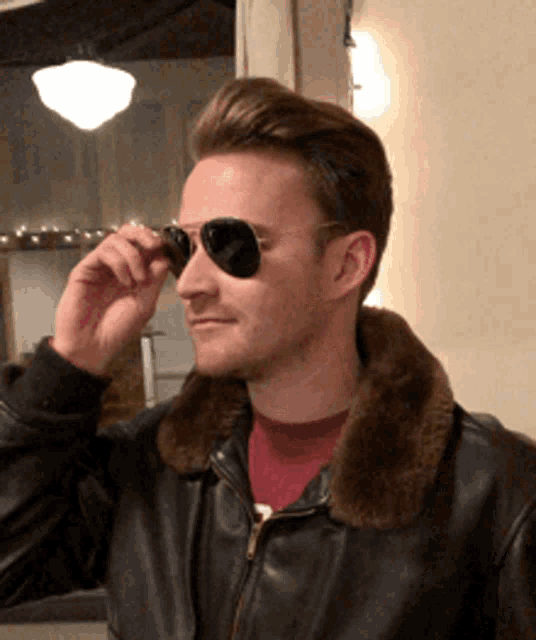 a man wearing a leather jacket and sunglasses adjusts his glasses