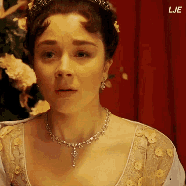 a close up of a woman wearing a necklace and a tiara with the letters lje below her