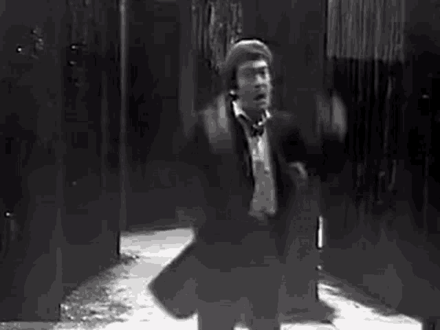 a man in a suit and tie is standing in a hallway with his arms outstretched in a black and white photo .