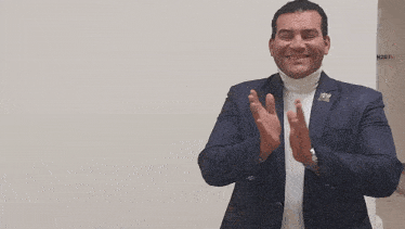 a man in a suit salutes in front of a white wall with k307 written on it
