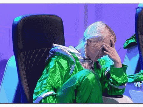 a woman in a green jacket sits in a chair with her hand to her face