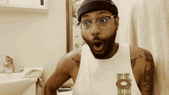 a man wearing glasses and a tank top with the number 8 on it looks surprised