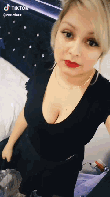 a woman in a black dress with a plunging neckline is taking a selfie .