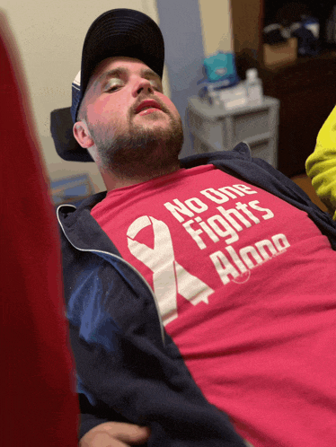 a man is wearing a pink shirt that says no one fights alone
