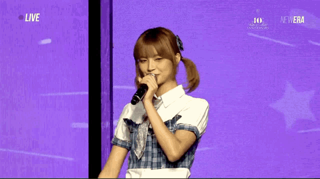 a girl singing into a microphone in front of a purple screen that says live
