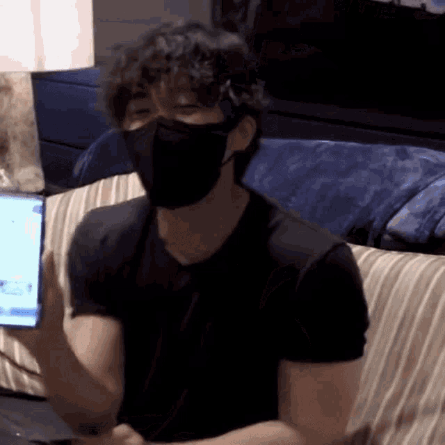 a man wearing a mask is sitting on a couch with a laptop