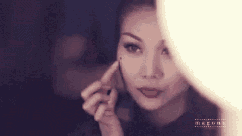 a woman is applying makeup in front of a mirror and looking at herself .