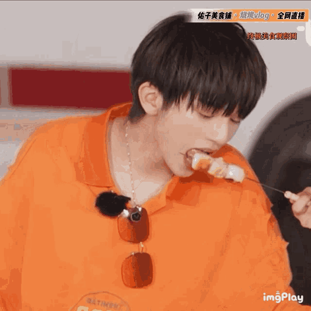 a young man wearing an orange shirt is eating something