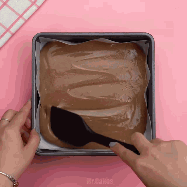 a person is using a spatula to spread chocolate in a square pan