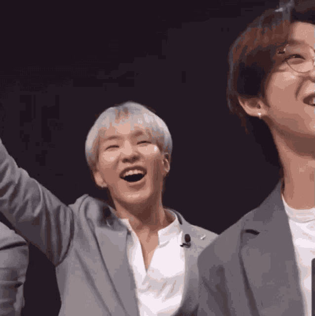 a man in a suit is laughing while standing next to another man in a white shirt