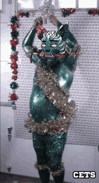 a green cat with christmas decorations and the word cets on the bottom right