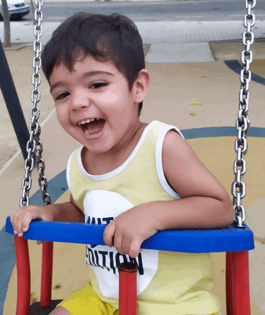 a young boy wearing a yellow tank top that says ' enthusiasm ' on it sits on a swing