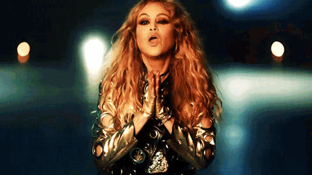 a woman with long curly hair is singing into a microphone in a dark room