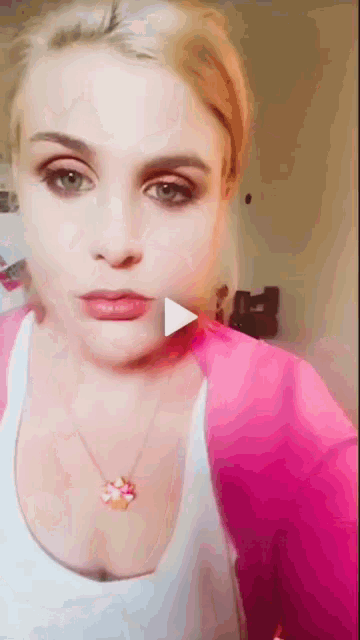 a woman wearing a pink jacket and a white tank top has a play button on her neck