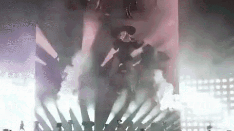 a group of people are standing on top of a stage surrounded by smoke and lights .