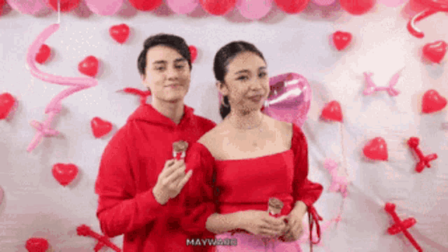 a man and a woman are posing for a picture with balloons in the background and maywood is written on the bottom right