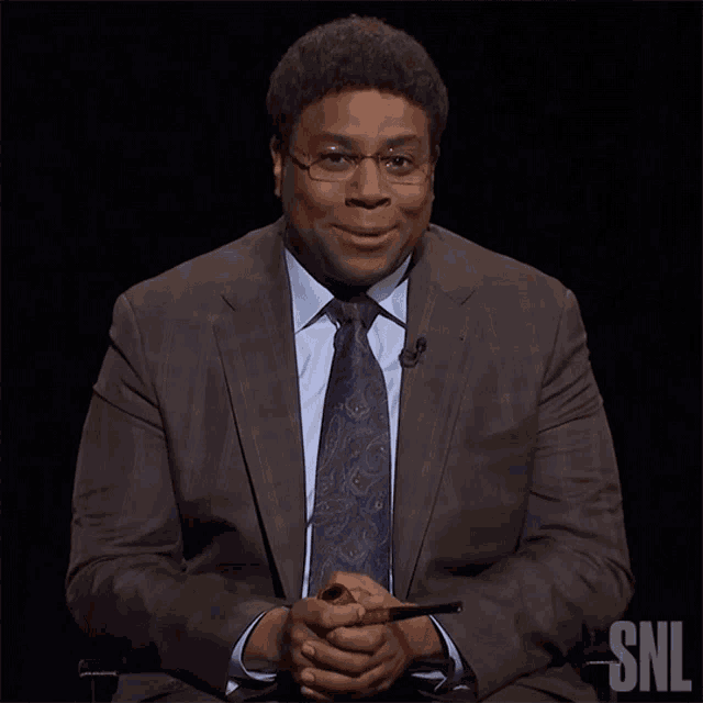 a man in a suit and tie sits in front of a snl sign