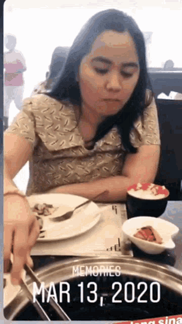 a woman is sitting at a table with a plate of food and a bowl of rice .