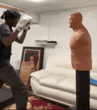 a man wearing boxing gloves stands in front of a mannequin
