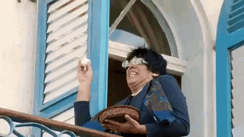 a woman is standing on a balcony holding a wicker basket and a egg .