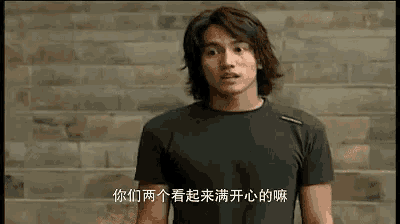 a man with long hair is standing in front of a brick wall and talking in a foreign language .