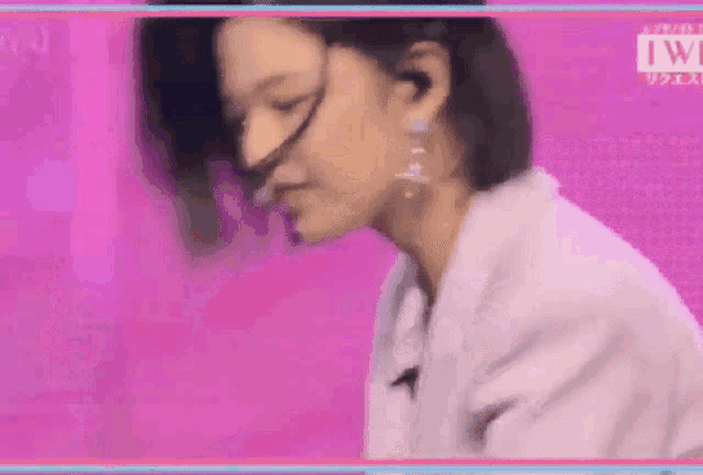 a woman in a white jacket is standing in front of a pink wall .