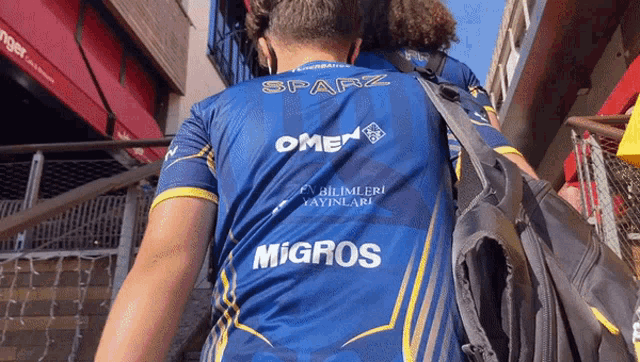 a man wearing a blue shirt with omen and migros on the back