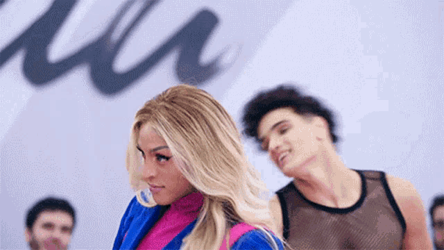 a woman in a blue jacket is standing in front of a man in a tank top .