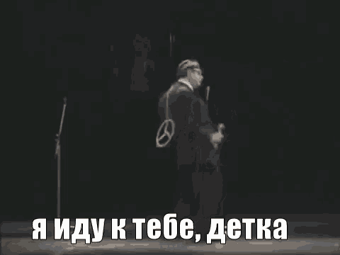 a man in a suit and tie is dancing on a stage in front of a microphone with a caption in russian