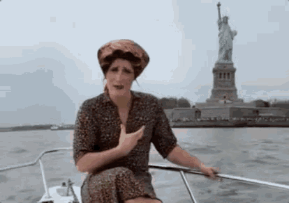 a woman is sitting in a boat in front of the statue of liberty .