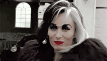 a woman with black and white hair and red lipstick is wearing a fur coat .