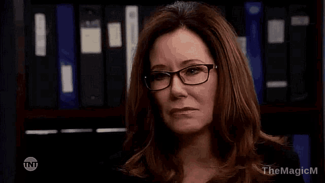 a woman wearing glasses is standing in front of a row of binders .